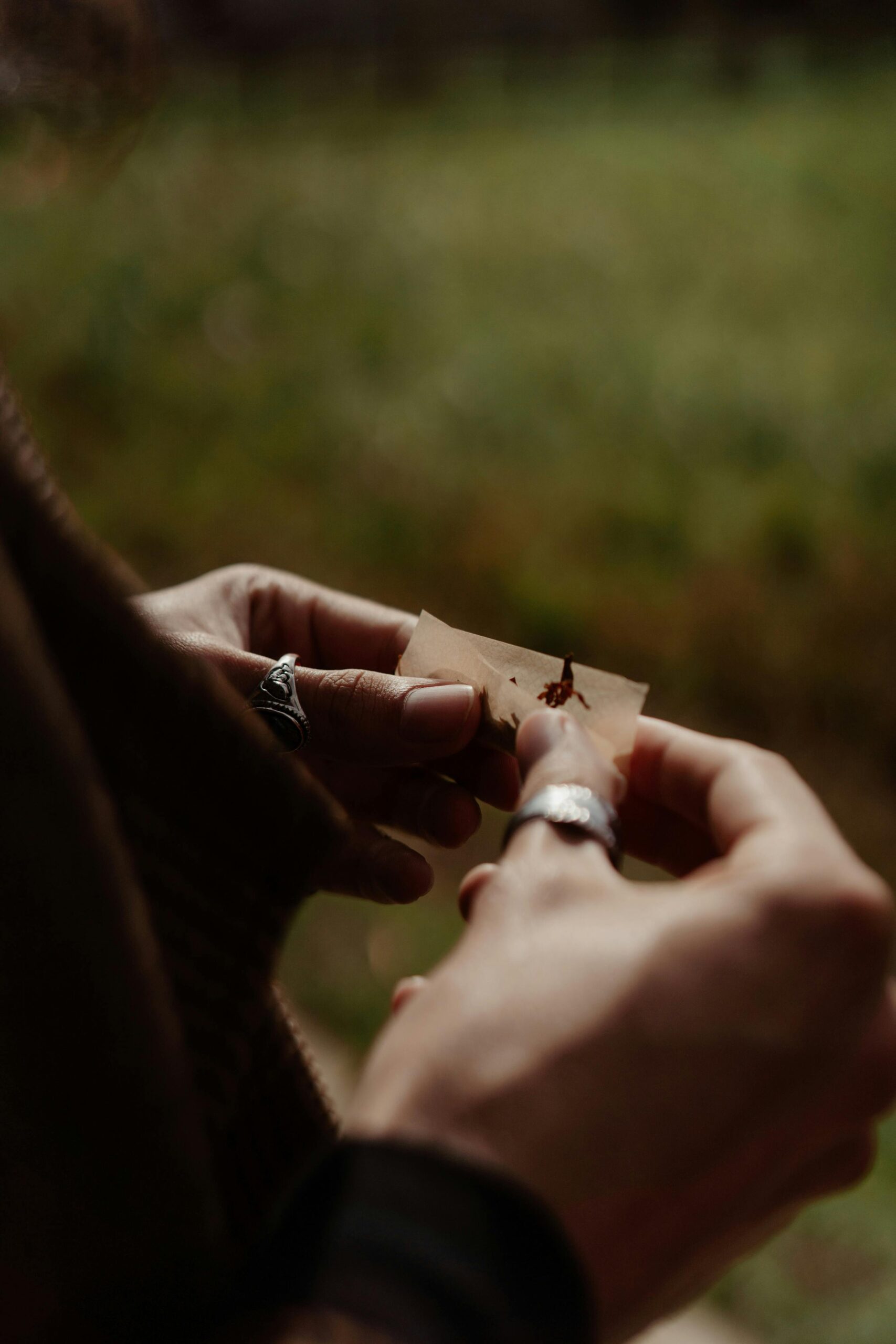 Detailed view of hands rolling a cigarette with natural background, showcasing skill and focus.