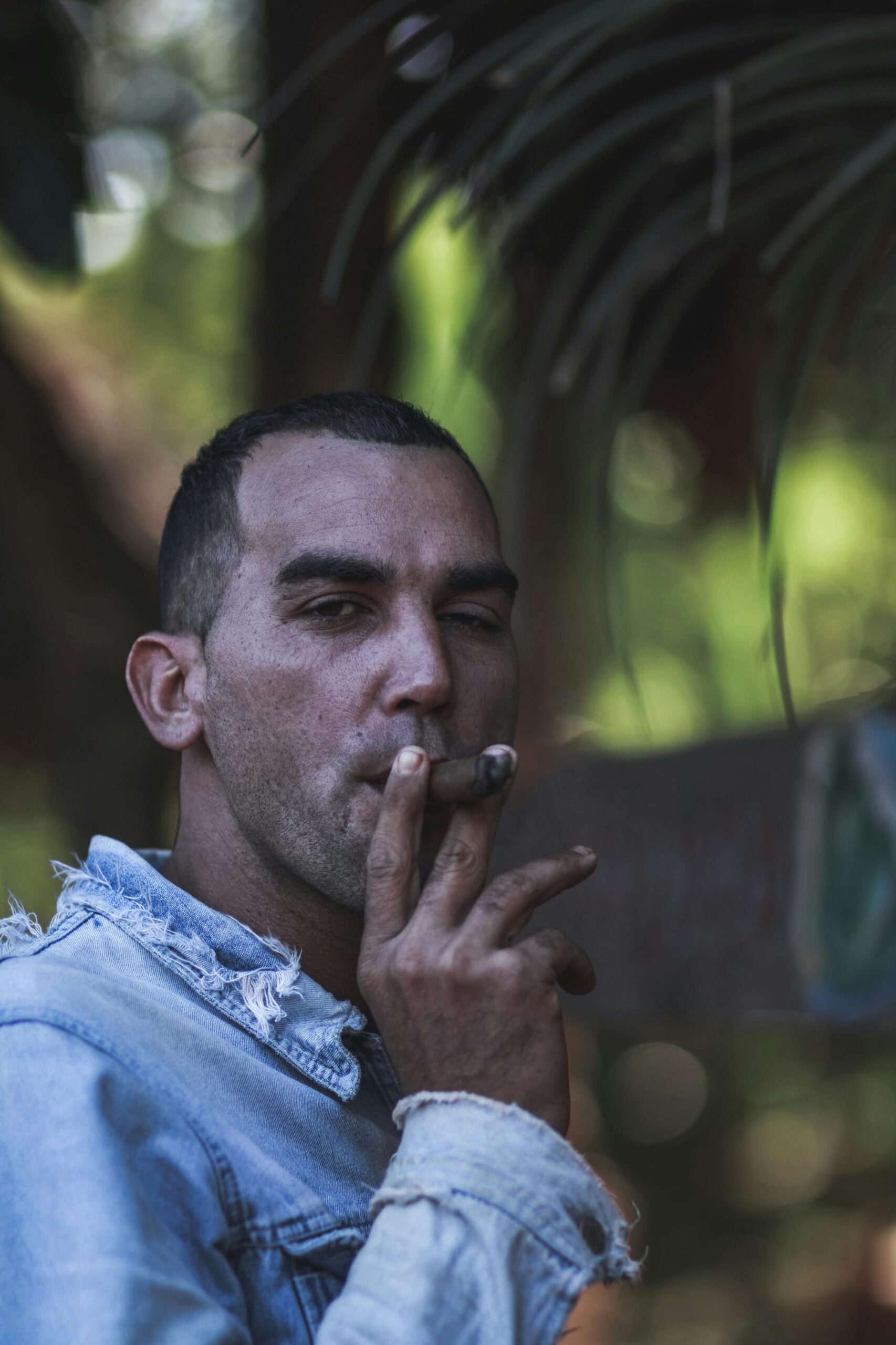Portrait of a man smoking a cigar while wearing a denim jacket outdoors.