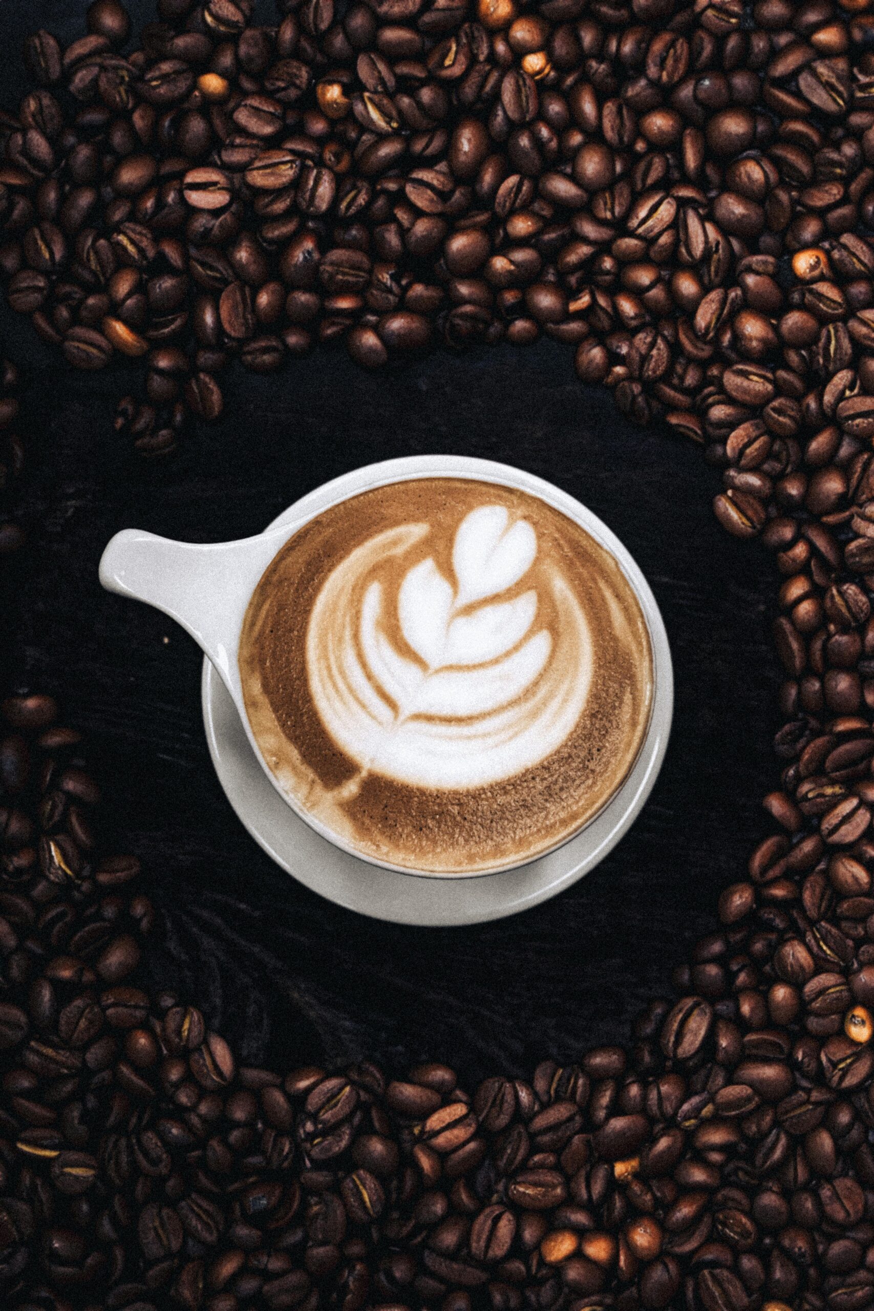 Top view of a frothy cappuccino with latte art surrounded by coffee beans.