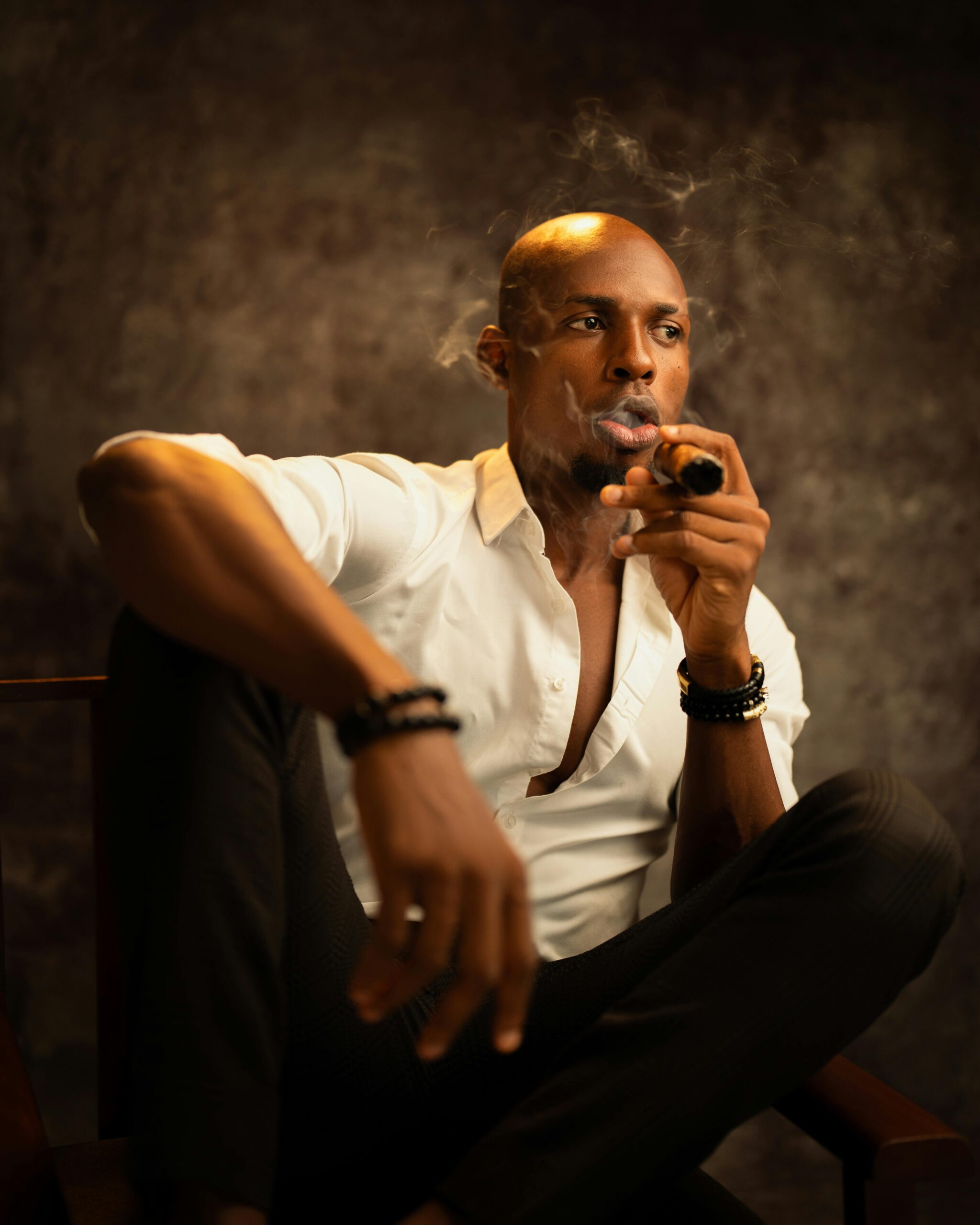 Elegant portrait of a bald man in white shirt smoking a cigar in a studio setting.