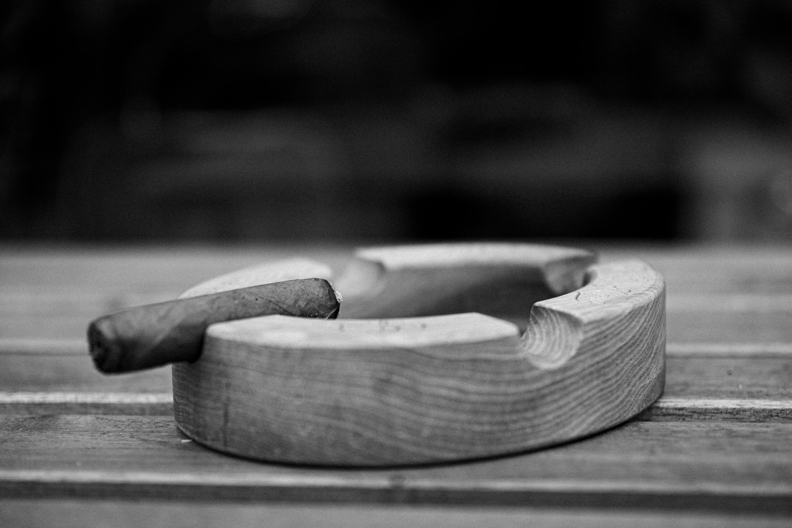 Monochrome image of a wooden ashtray with a cigar on a wooden table, highlighting texture.
