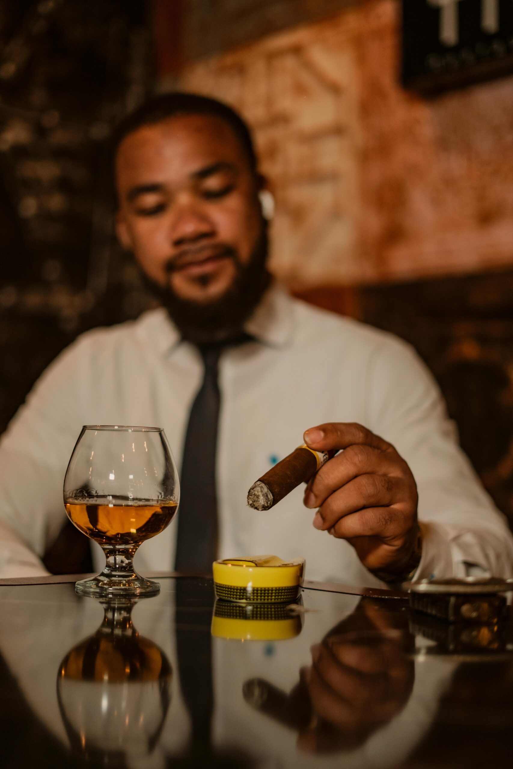 A sophisticated gentleman enjoys a cigar and brandy indoors, reflecting a moment of leisure.