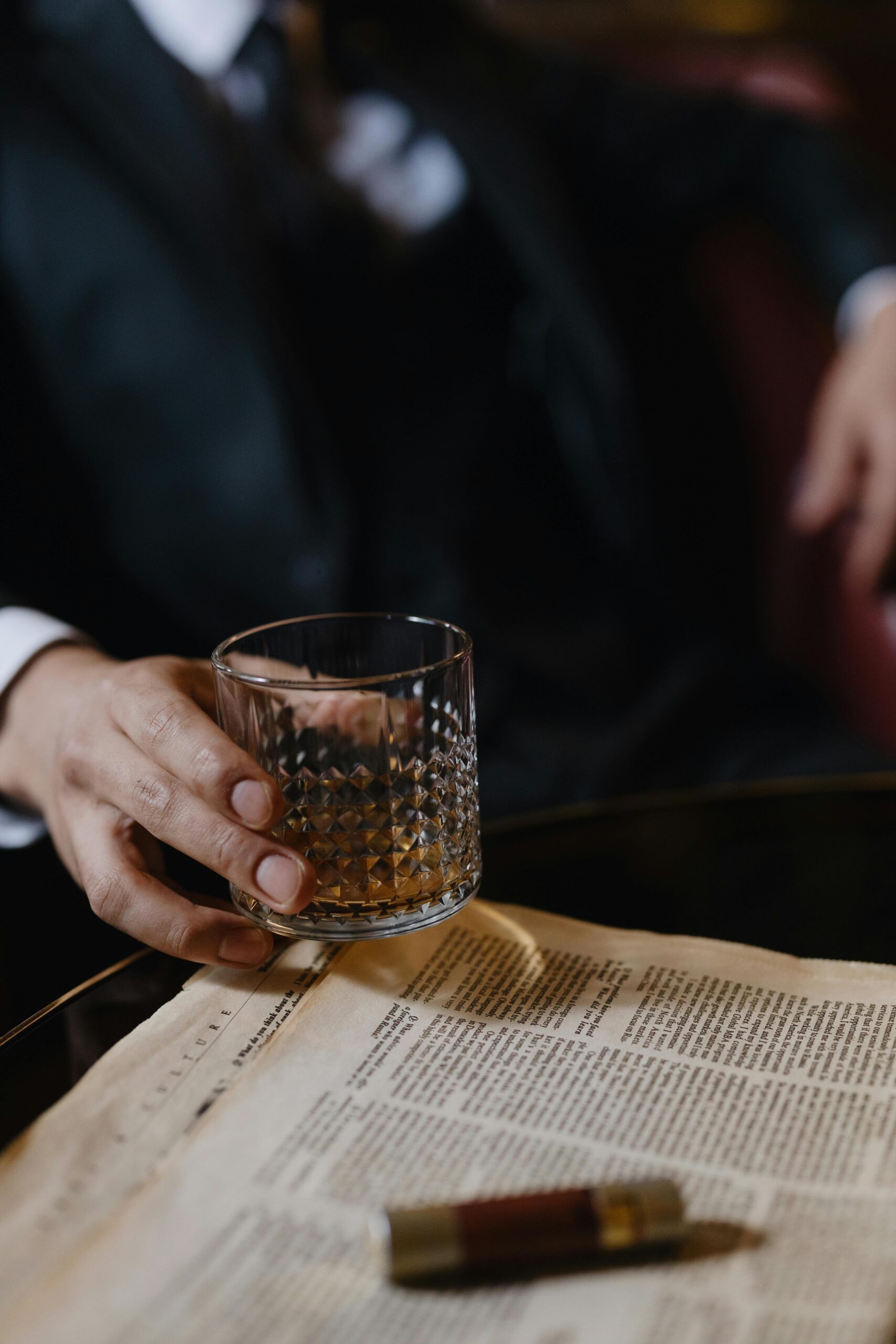 Sophisticated scene of a hand holding whiskey glass over a newspaper, capturing elegance.